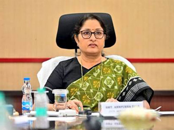 Annpurna Devi, in a green patterned sari, chairs a meeting at a conference table; her nameplate is in front of her
