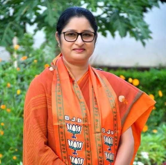 Portrait of Annpurna Devi in an orange sari and stole, standing in a garden with marigolds