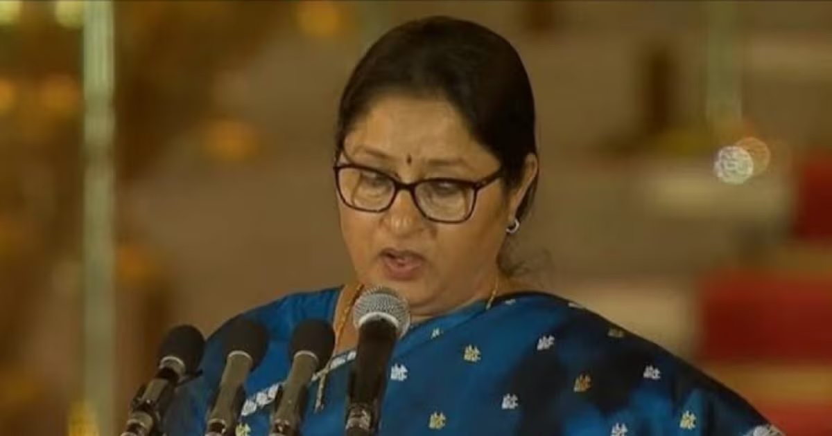 Annpurna Devi, in a blue silk sari and spectacles, reads the oath at a lectern with several microphones