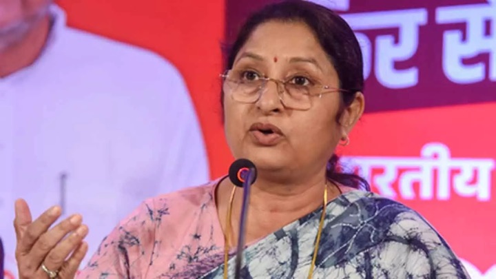 Annpurna Devi, in spectacles and a pink-and-indigo sari, speaks into a microphone, gesturing with her right hand