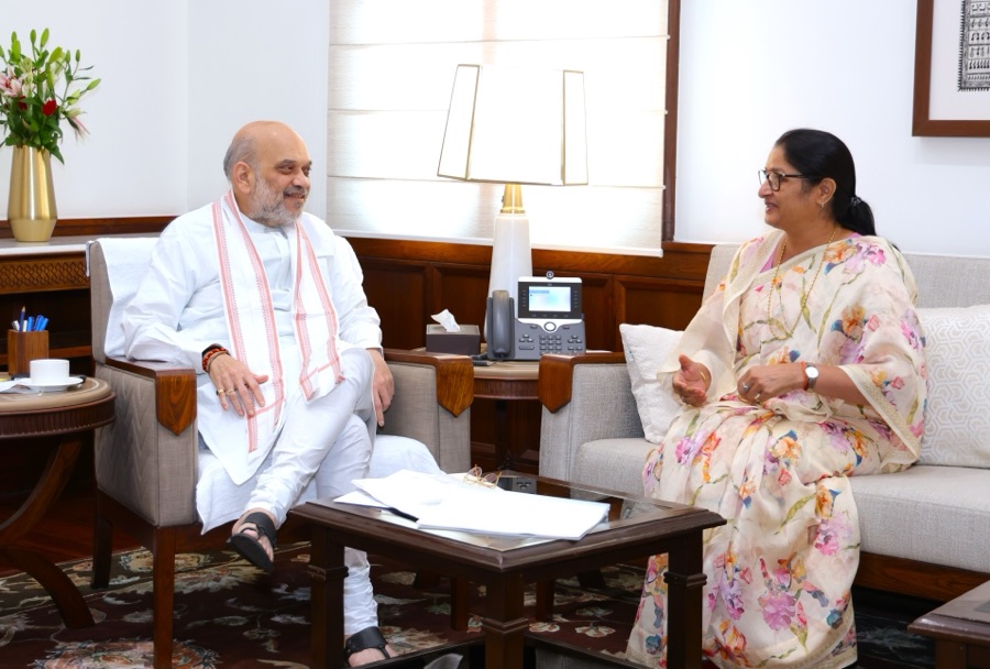 Annpurna Devi, seated on a sofa in a floral sari, speaks with Amit Shah, seated in an armchair, across a low table with papers